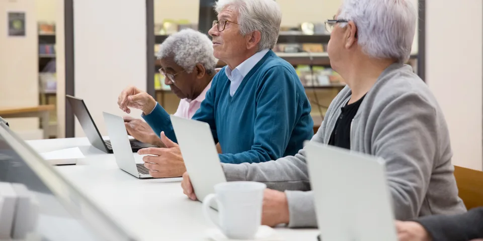 Drei Kursteilnehmer sitzen mit ihren Laptops an einem Tisch und schauen aufmerksam nach vorn.